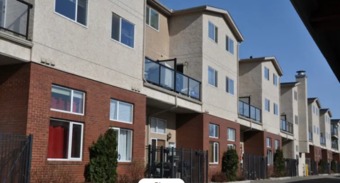 A row of apartment buildings with balconies and trees in front.