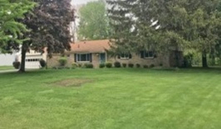A house with a green lawn and trees in the background.