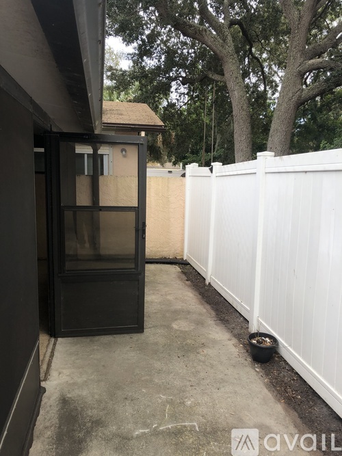 A white fence with a black door and a small building in the background.