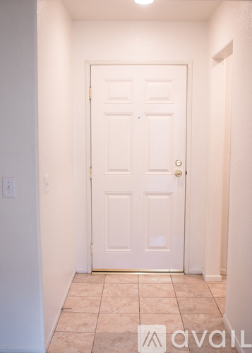 A white door with a gold handle is in a hallway with tiled flooring.