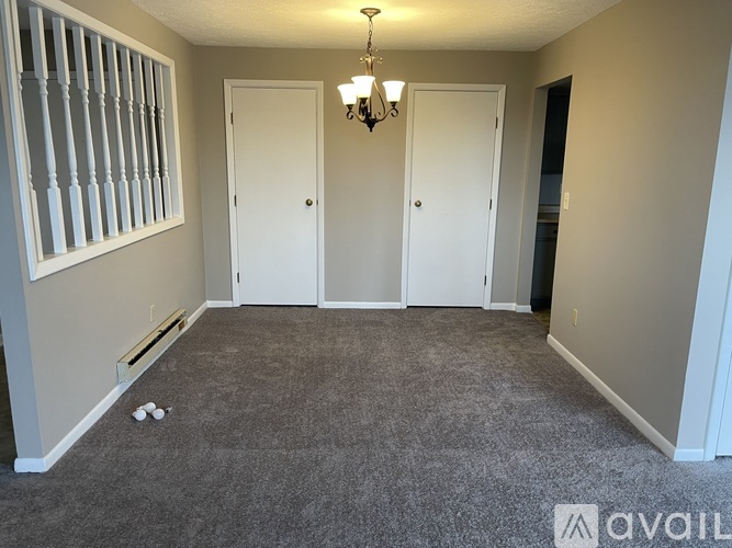 A room with a carpeted floor, two doors, and a window with bars on the left side.