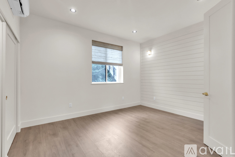 A spacious room with wooden flooring and a window with blinds.