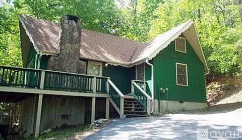 A green house with a porch and a chimney.