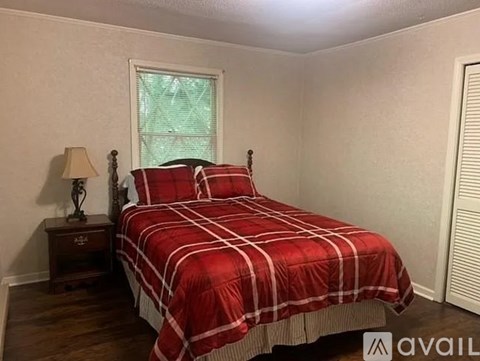 A bedroom with a red and white bedspread and a wooden nightstand with a lamp.