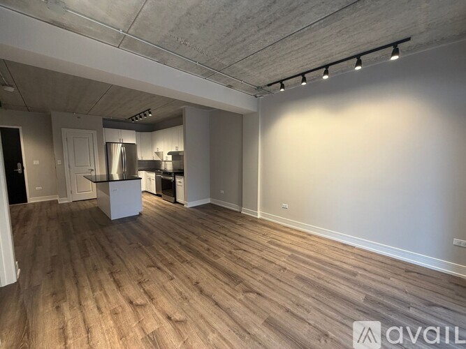 A spacious room with wooden flooring and a kitchen area in the background.