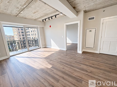 A spacious room with wooden flooring and a kitchen area in the background.