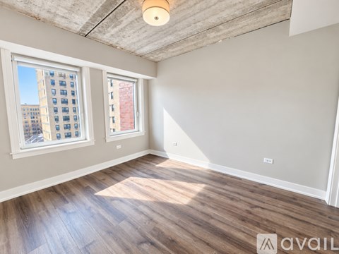 A spacious room with wooden flooring and a large window with a view of a building.