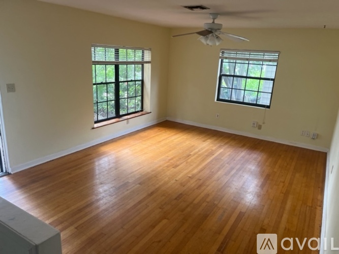 A room with wooden flooring and two windows.