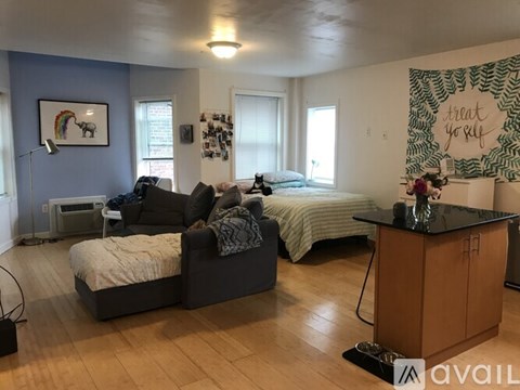 A living room with a grey couch and a bed with a green and white striped blanket.
