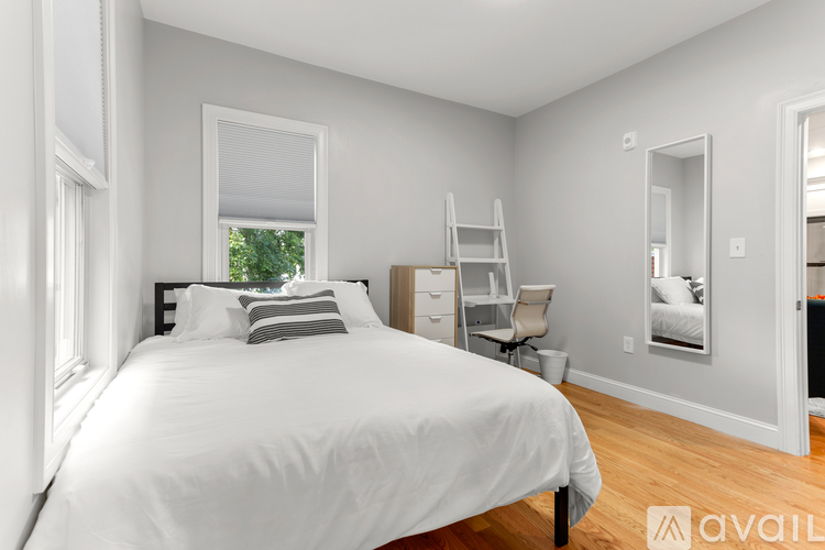 A bedroom with a white bed and a window with blinds.