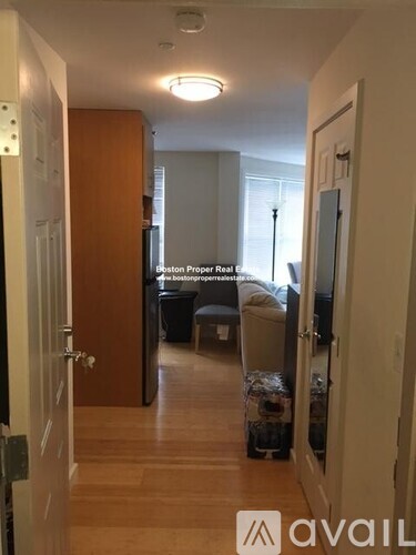 A hallway with a door on the left and a bedroom with a bed and a couch in the background.