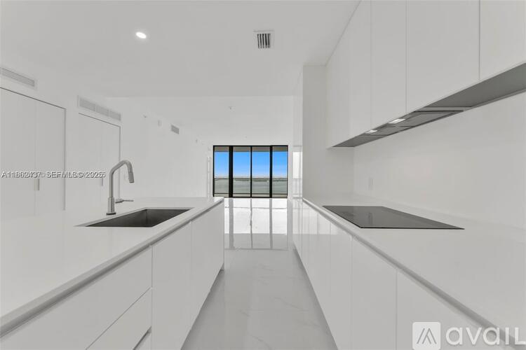A modern kitchen with white cabinets and a large window.