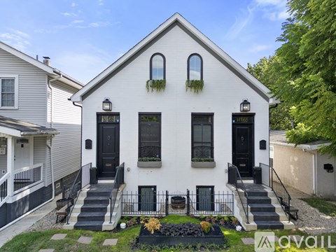 A white house with black doors and windows is surrounded by a black metal fence.