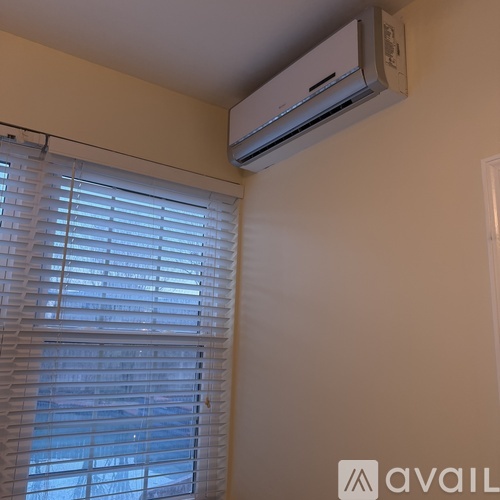 A wall-mounted air conditioner is above a window with blinds.