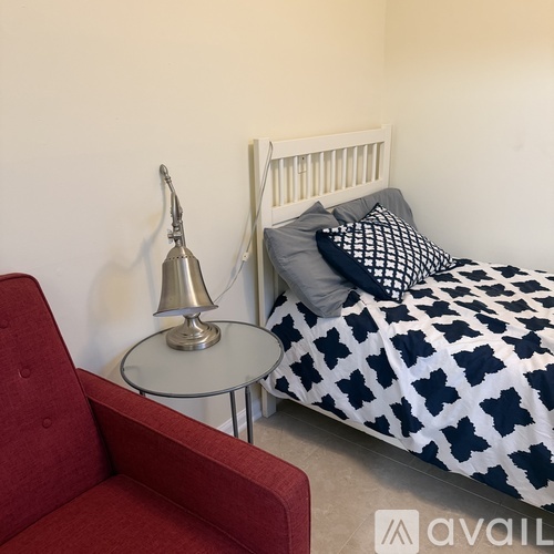 A bedroom with a bed, a red chair, and a bedside table with a lamp.