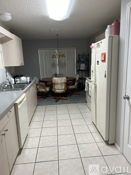 A kitchen with a white fridge and a dining table with chairs.