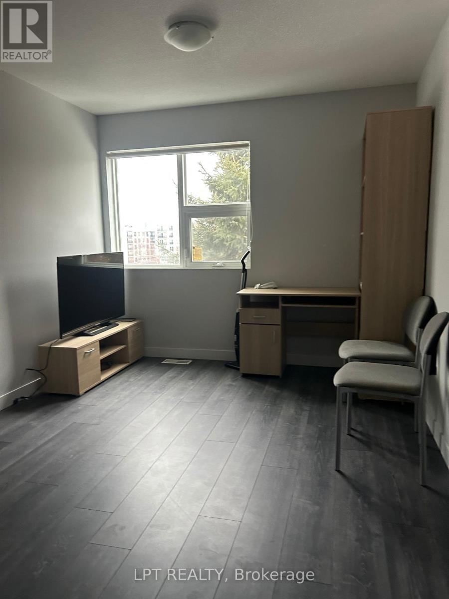 A room with a grey floor and a window with a view of trees and buildings outside.