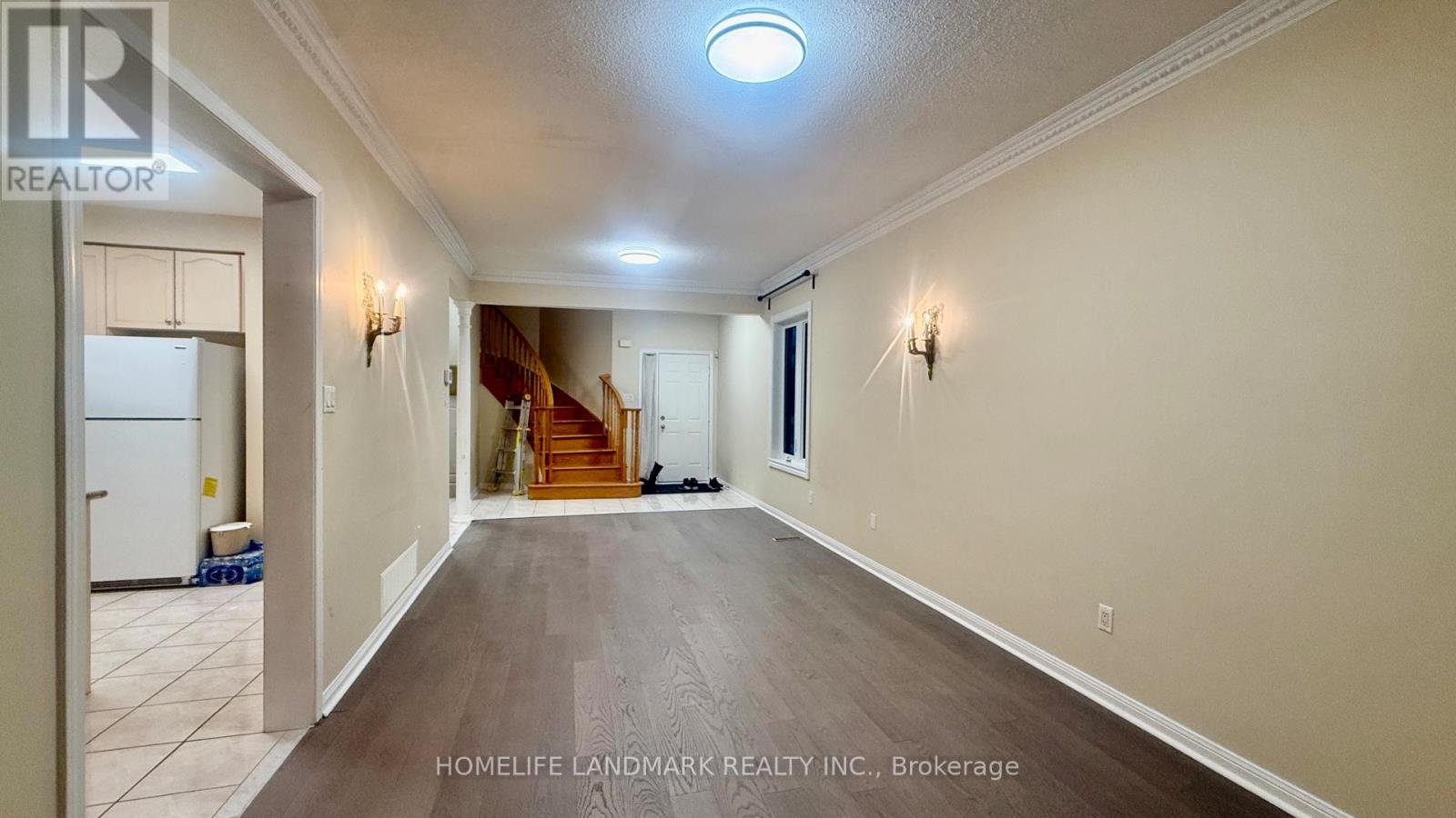 A spacious hallway with a refrigerator on the left and a staircase in the background.