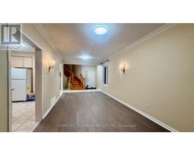 A spacious hallway with a refrigerator on the left and a staircase in the background.