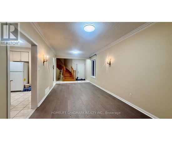 A spacious hallway with a refrigerator on the left and a staircase in the background.