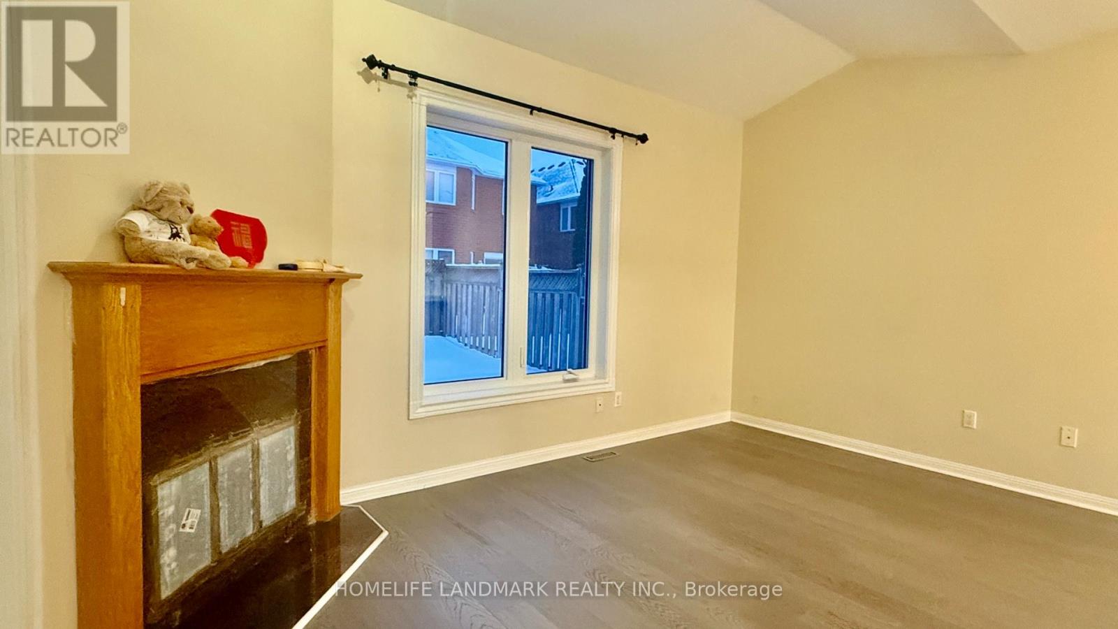 A room with a fireplace and a window with a view of a fence and buildings outside.