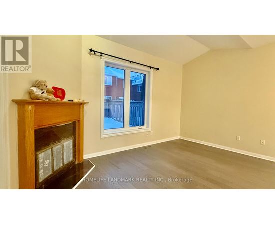 A room with a fireplace and a window with a view of a fence and buildings outside.