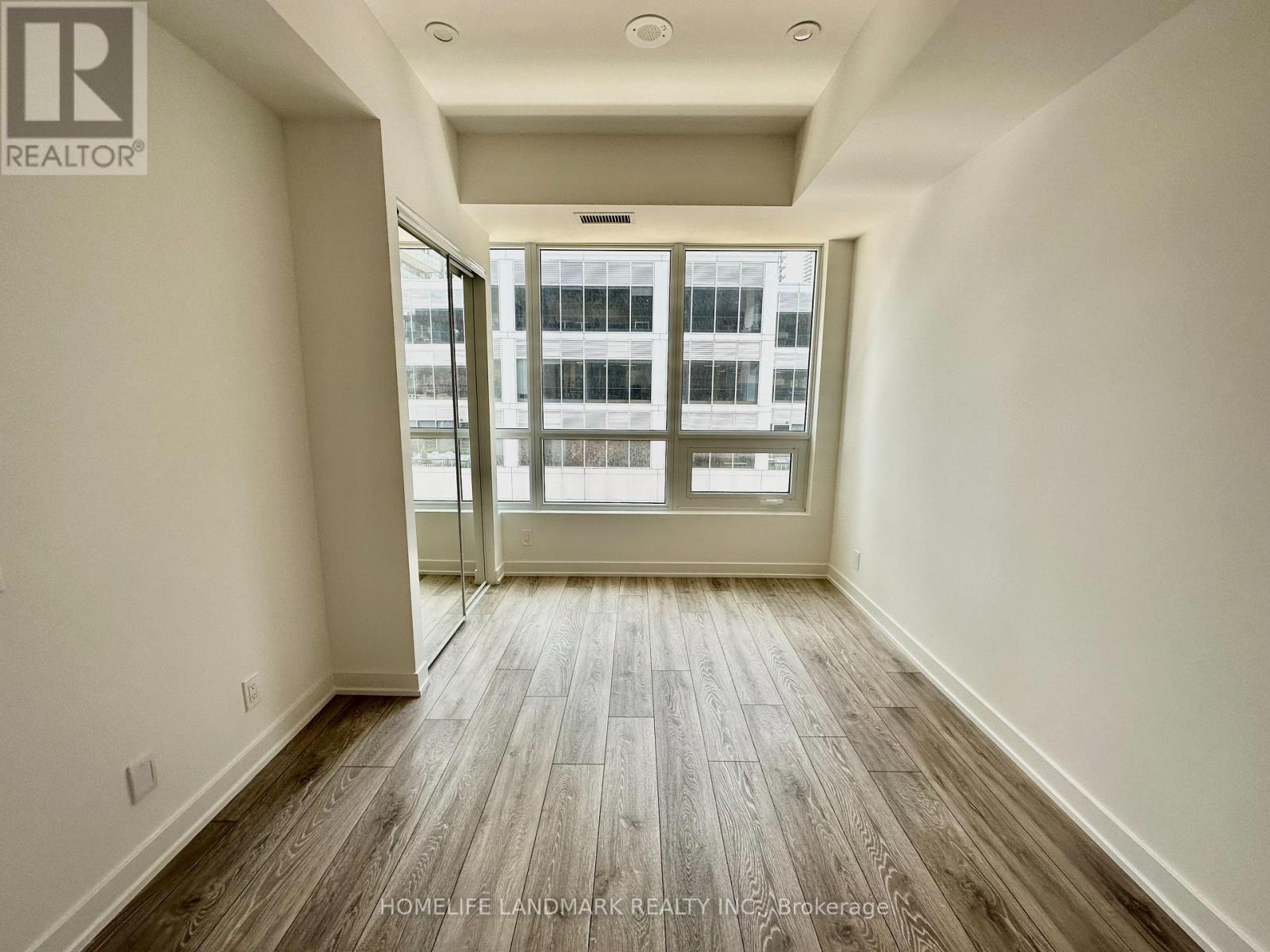 A spacious room with wooden flooring and a sliding glass door leading to a balcony.