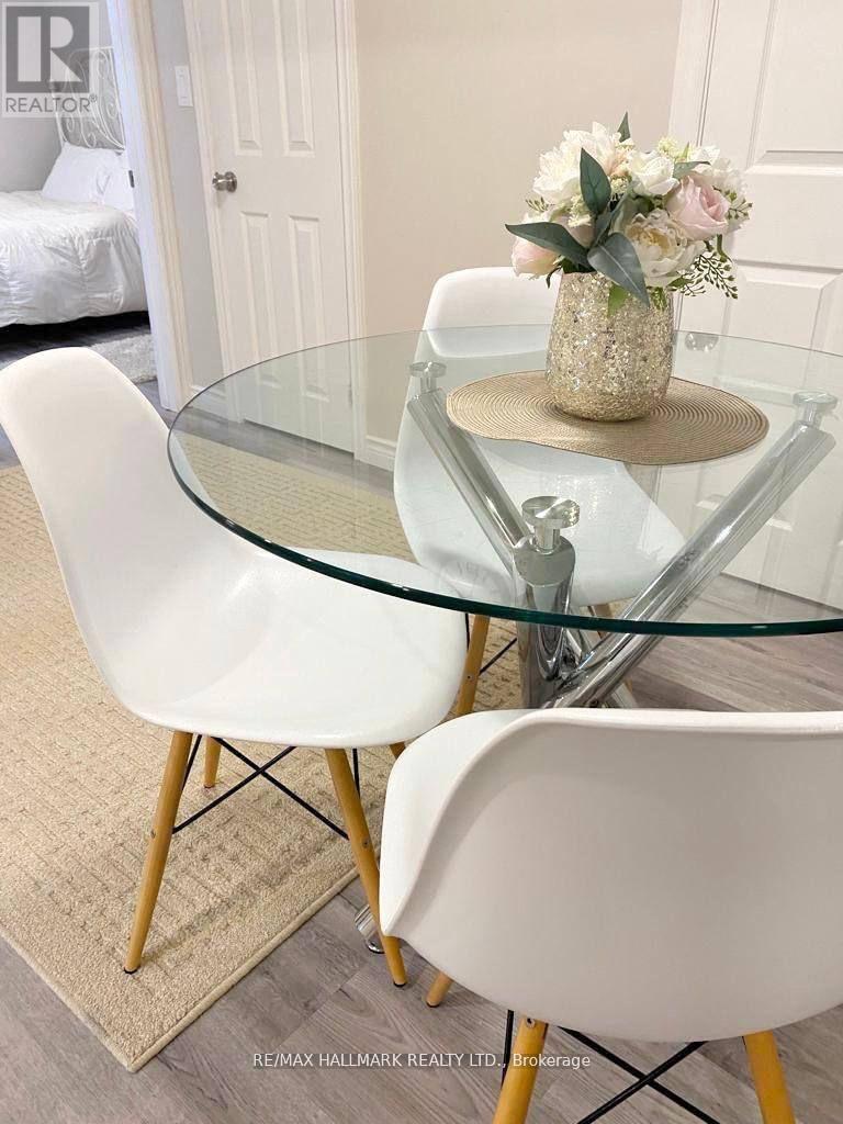 A glass table with a floral arrangement in a gold vase sits between two white chairs.