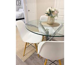 A glass table with a floral arrangement in a gold vase sits between two white chairs.