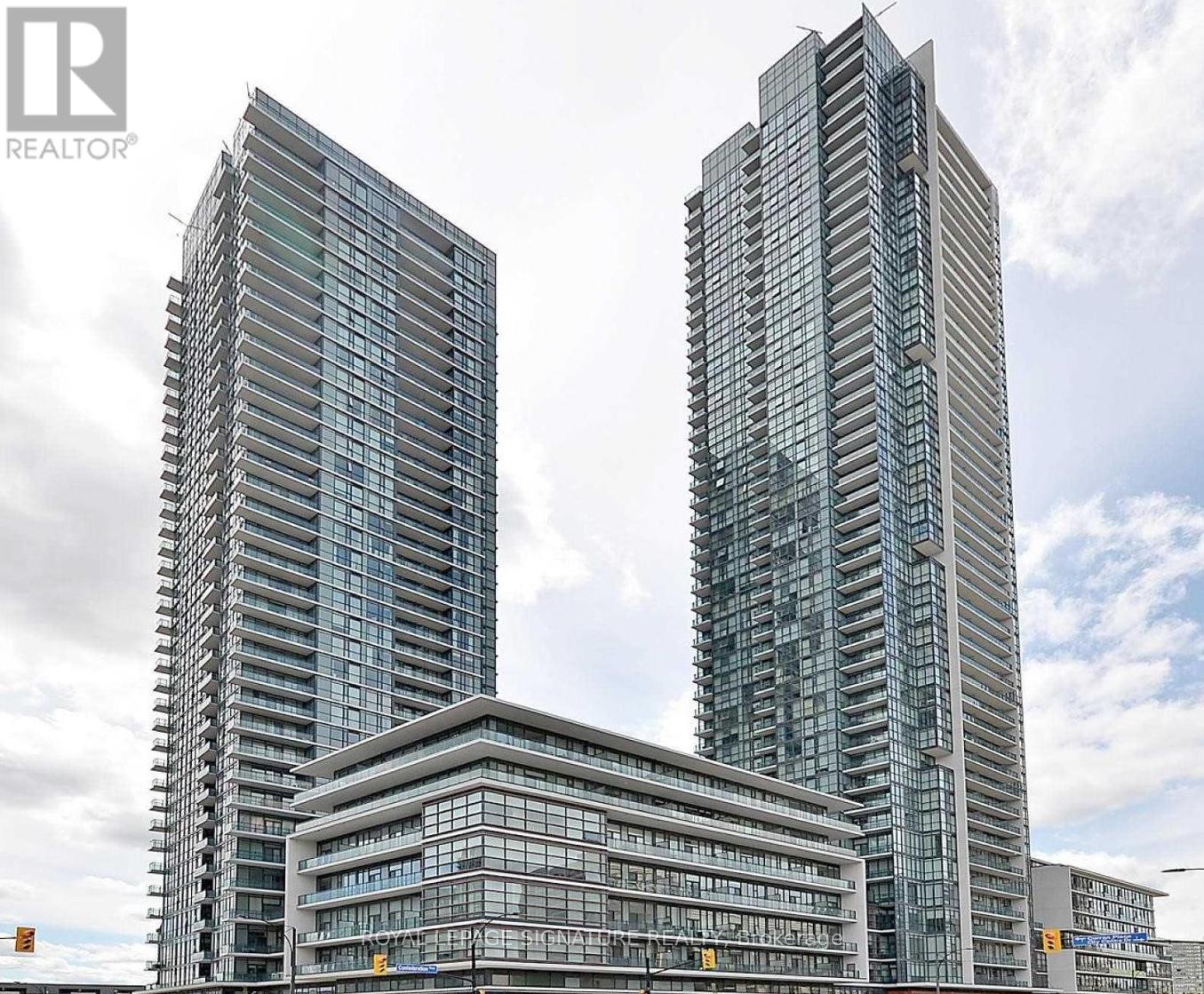 Two tall buildings with glass windows are in the foreground with a cloudy sky in the background.