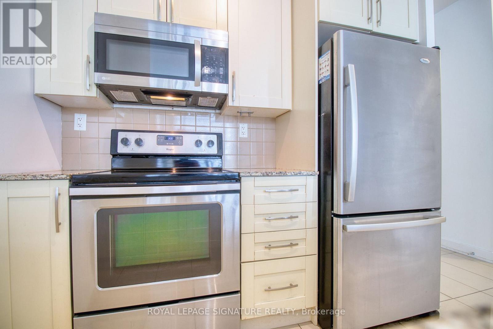 A stainless steel refrigerator stands next to a stove and microwave in a kitchen.