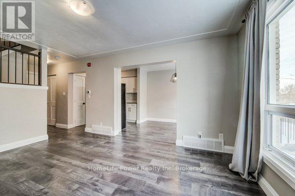 A spacious room with a grey floor and white walls, featuring a window with curtains and a doorway leading to another room.