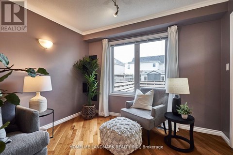 A living room with a grey ottoman, two grey chairs, and a table with a lamp on it.