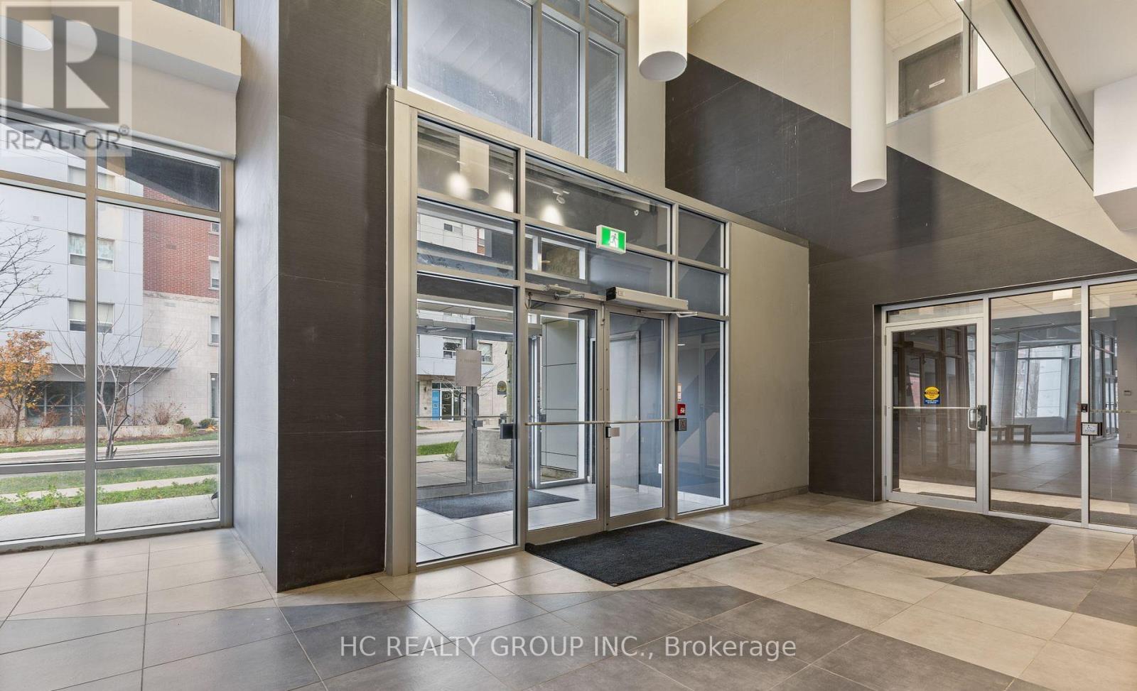 The image shows the entrance to a building with glass doors and a sign that reads "HC REALTY GROUP INC., Brokerage."