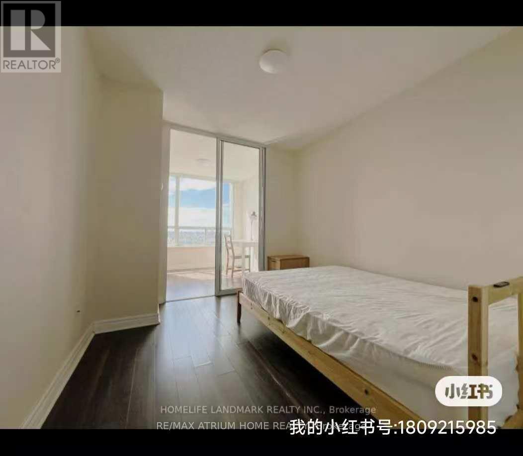 A bedroom with a bed, wooden floors, and a sliding glass door leading to a balcony.