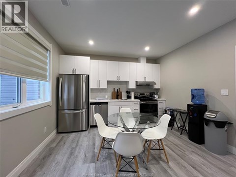 A kitchen with a refrigerator, dining table, and chairs.