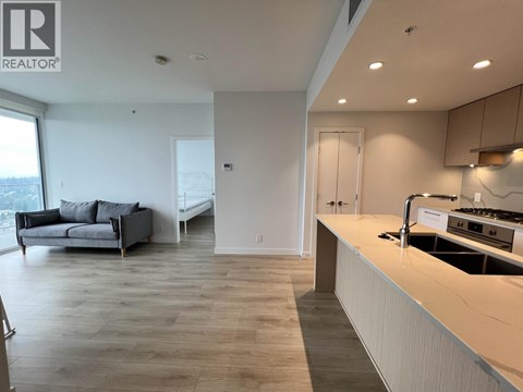 A modern kitchen with a large island and a living area with a couch and a window.