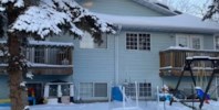 A snow covered tree in front of a blue house.