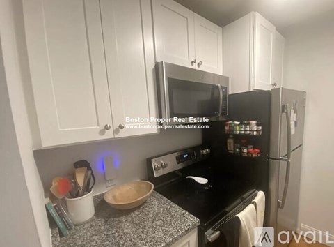 A kitchen with white cabinets and black appliances is available for rent.
