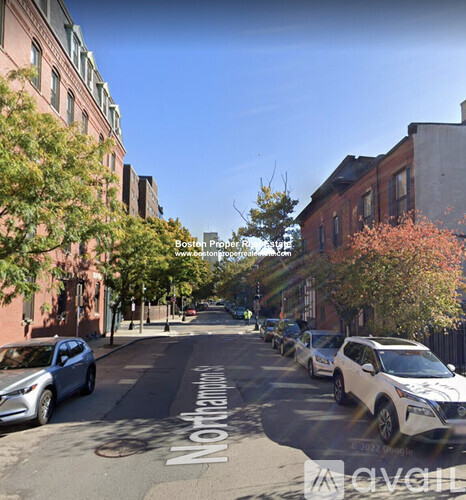 A street view with cars parked on the side and buildings on both sides.