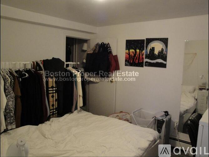 A bedroom with a bed, clothes hanging on a rack, and a poster on the wall.