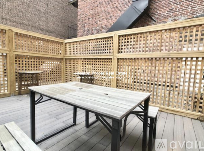A wooden table and bench are on a deck with lattice fencing.