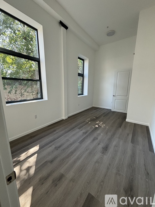 A room with wooden flooring and two windows.