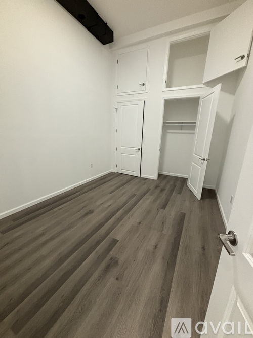 A room with white walls and wood flooring, featuring a white door and a white cabinet.