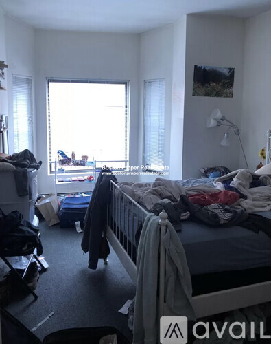 A messy bedroom with a bed, chair, and window.