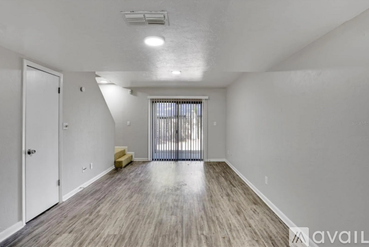 A room with a white door, a window with blinds, and a wooden floor.