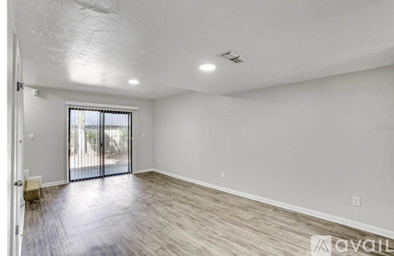 A spacious room with wooden flooring and a sliding glass door leading outside.