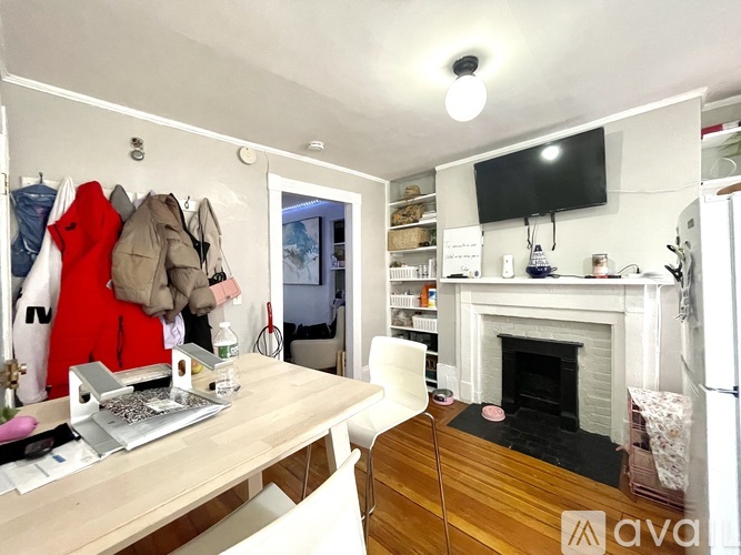 A room with a fireplace, a TV, and a desk with clothes hanging on it.