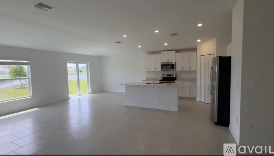 A spacious, empty room with a kitchen area in the background.