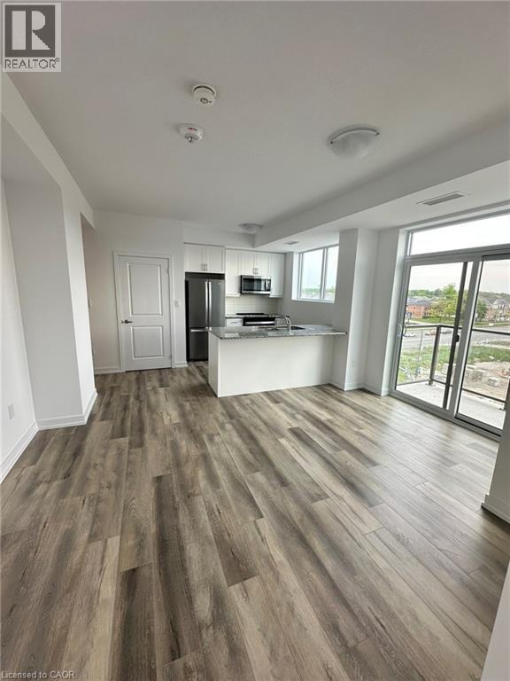 A spacious room with wood flooring and a kitchen area in the background.